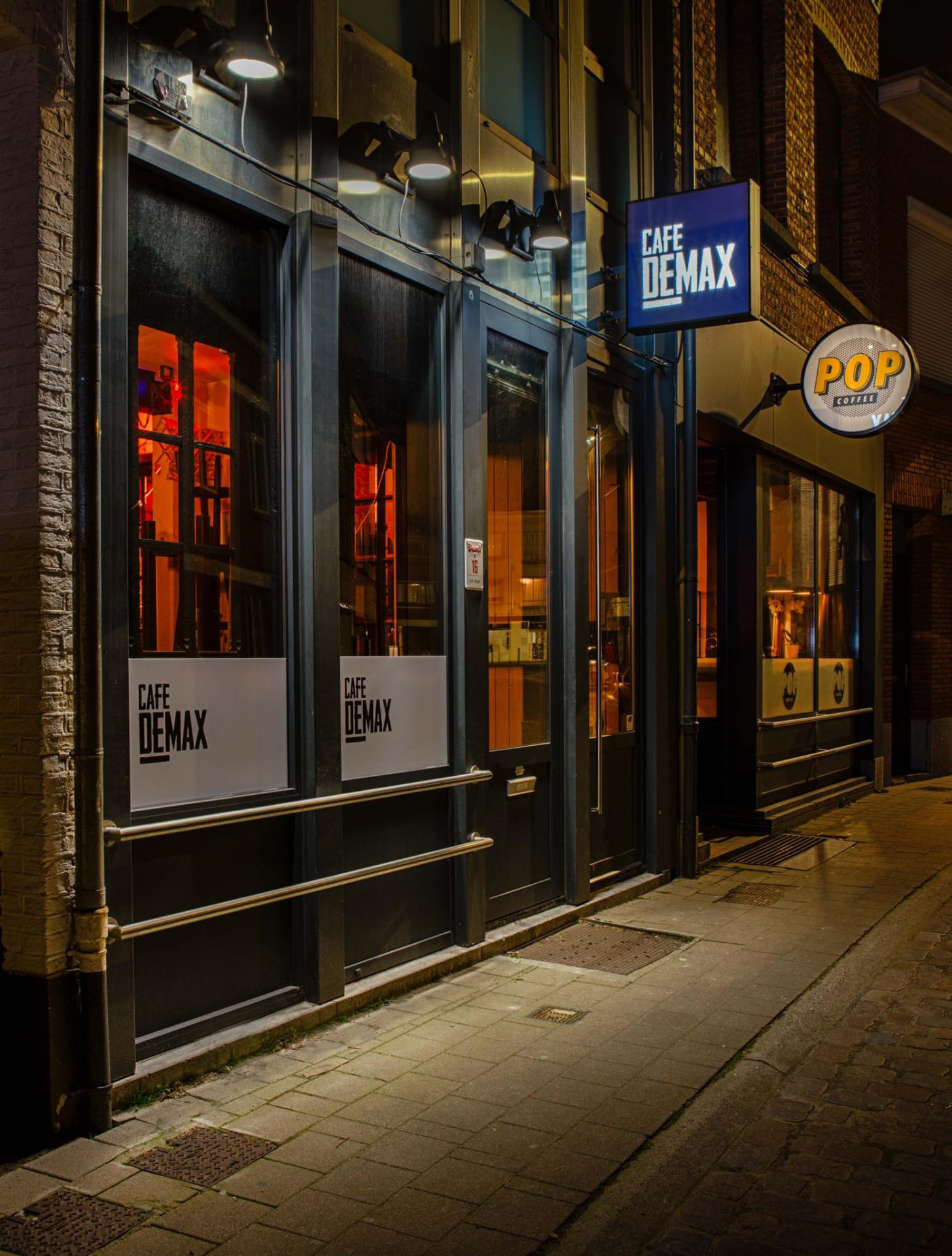 De gevel van Café De Max 's avonds, verlicht van binnenuit